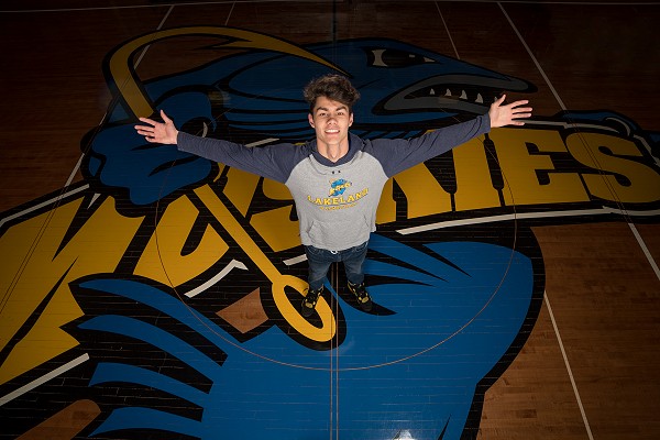 Lakeland student with arms out on Muskies logo on basketball court.