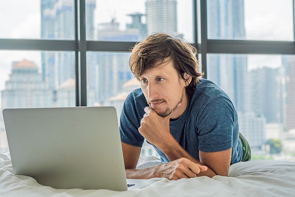 Young man is working on a laptop in his bed.